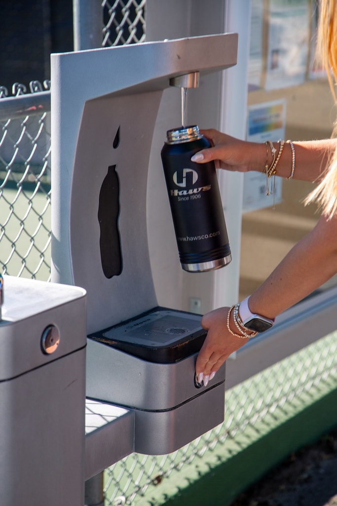 Person filling a water bottle at an outdoor Haws hydration station